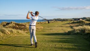A junior golfer completes a full driver swing follow-through on a dramatic links-style golf course with coastal dunes and ocean views in the background, showcasing the explosive rotational power and balanced finish position that result from a dedicated junior golf core training program.